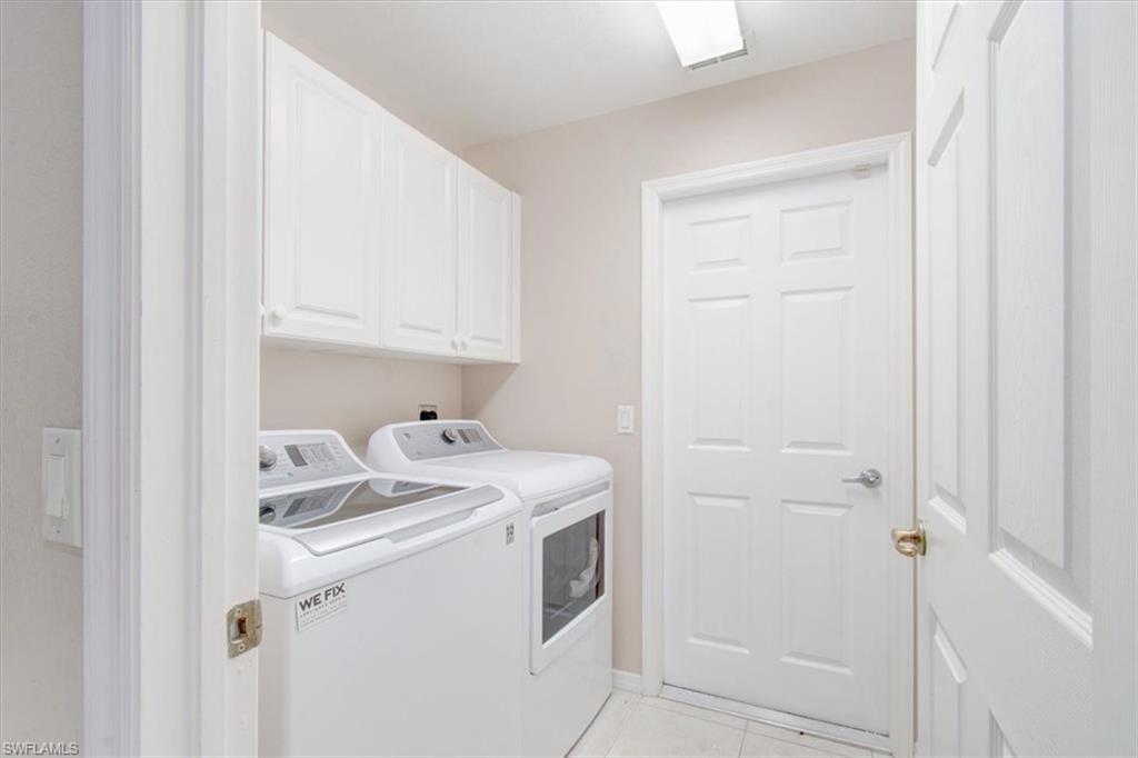 Laundry area featuring light tile patterned flooring, cabinet space, and washing machine and clothes dryer