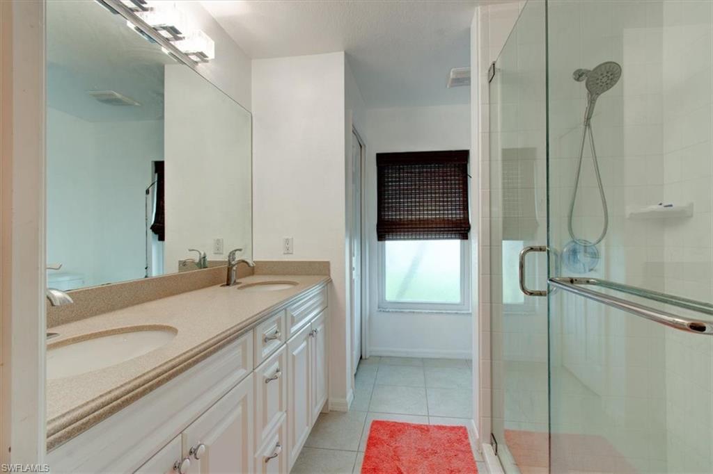 Bathroom with double vanity, light tile patterned floors, and a stall shower