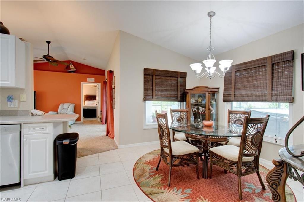 Dining space with lofted ceiling, a chandelier, light tile patterned floors, and light carpet