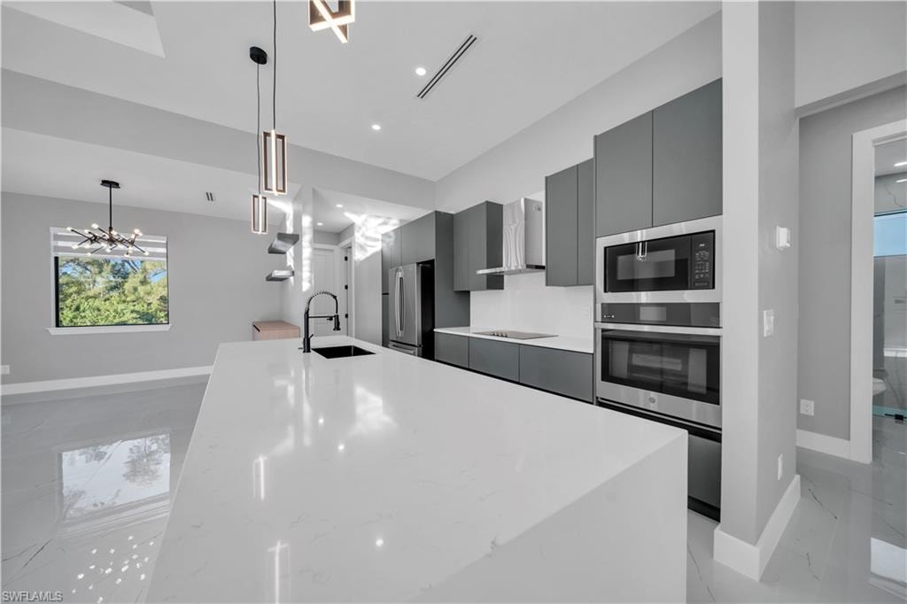 Kitchen featuring an island with sink, modern cabinets, appliances with stainless steel finishes, wall chimney exhaust hood, and gray cabinets