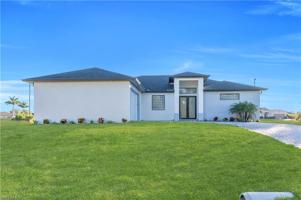 Prairie-style home with a front yard, stucco siding, decorative driveway, and a shingled roof