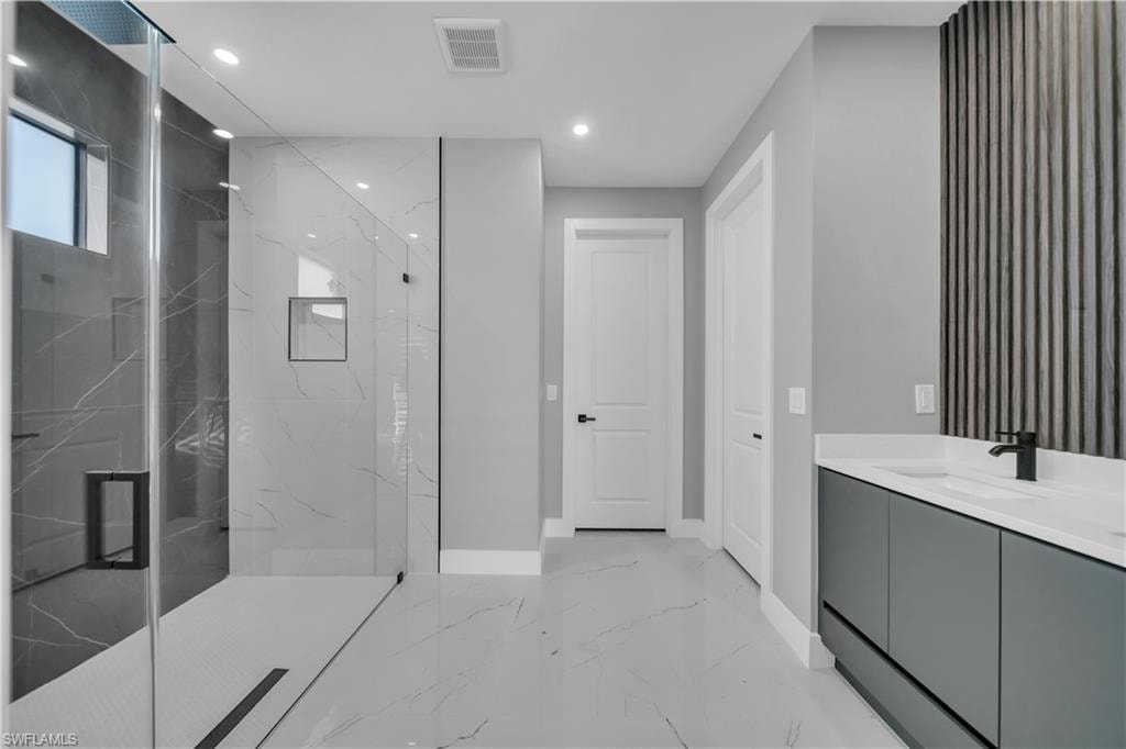 Bathroom with vanity, a marble finish shower, recessed lighting, and light marble finish flooring
