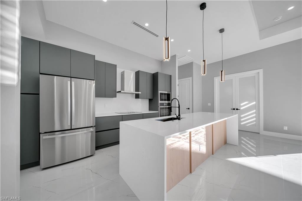 Kitchen featuring stainless steel appliances, light marble finish floors, an island with sink, decorative light fixtures, and recessed lighting