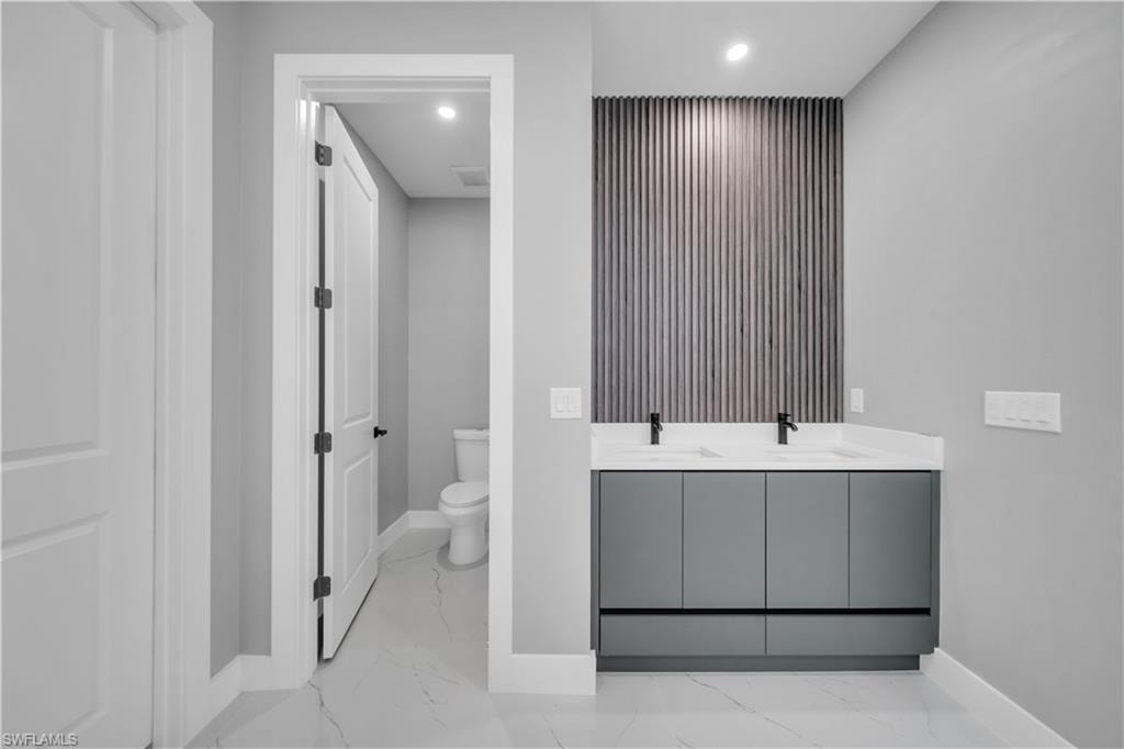 Full bath with recessed lighting, double vanity, and light marble finish floors