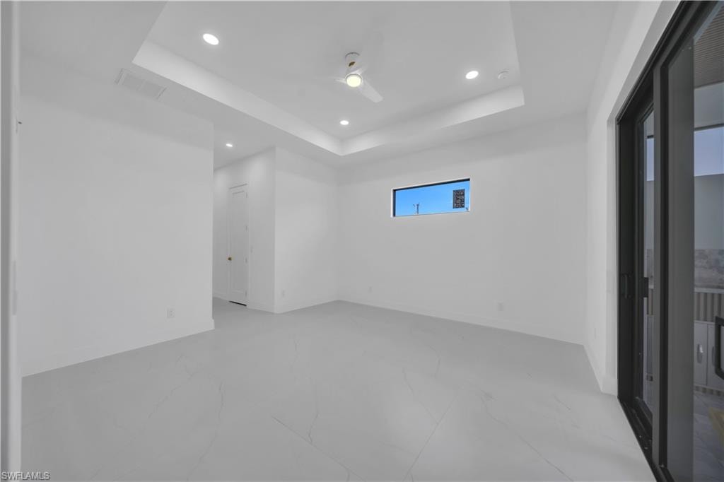 Master bed room featuring light-toned flooring, a tray ceiling with recessed lighting, and a ceiling fan