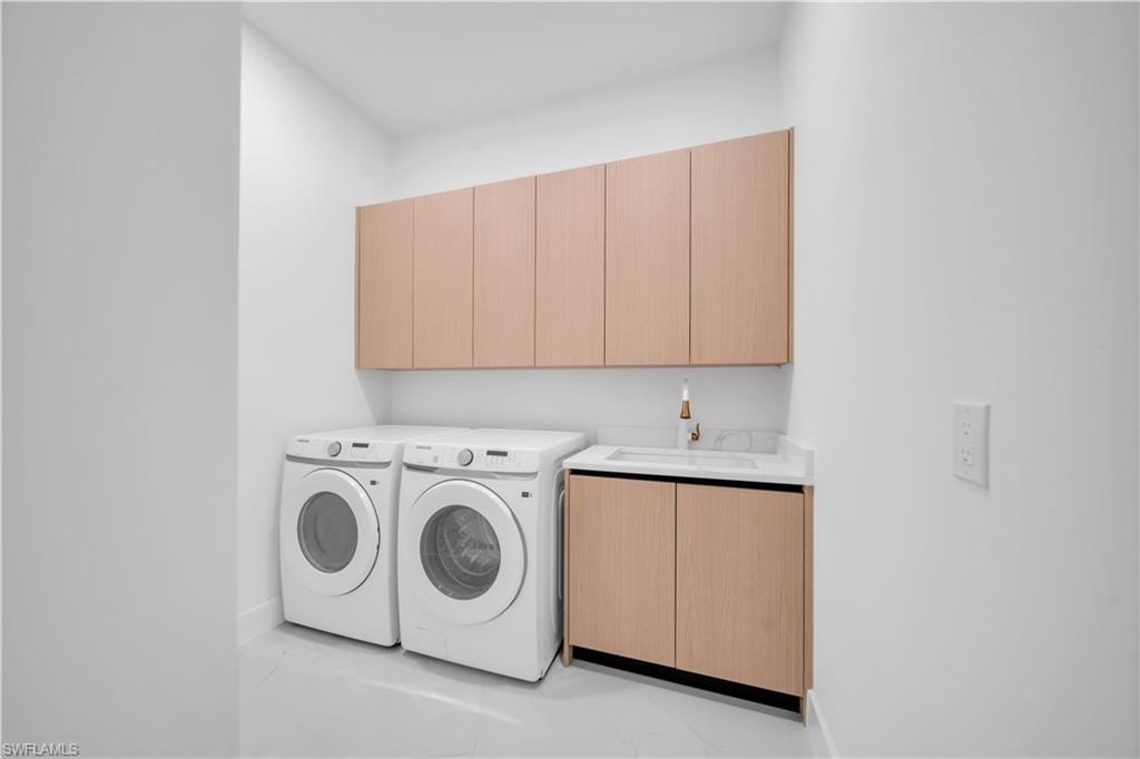 Dedicated utility space featuring light wood-finish cabinetry, a built-in sink with a gold-tone faucet, a white countertop, and clean white walls