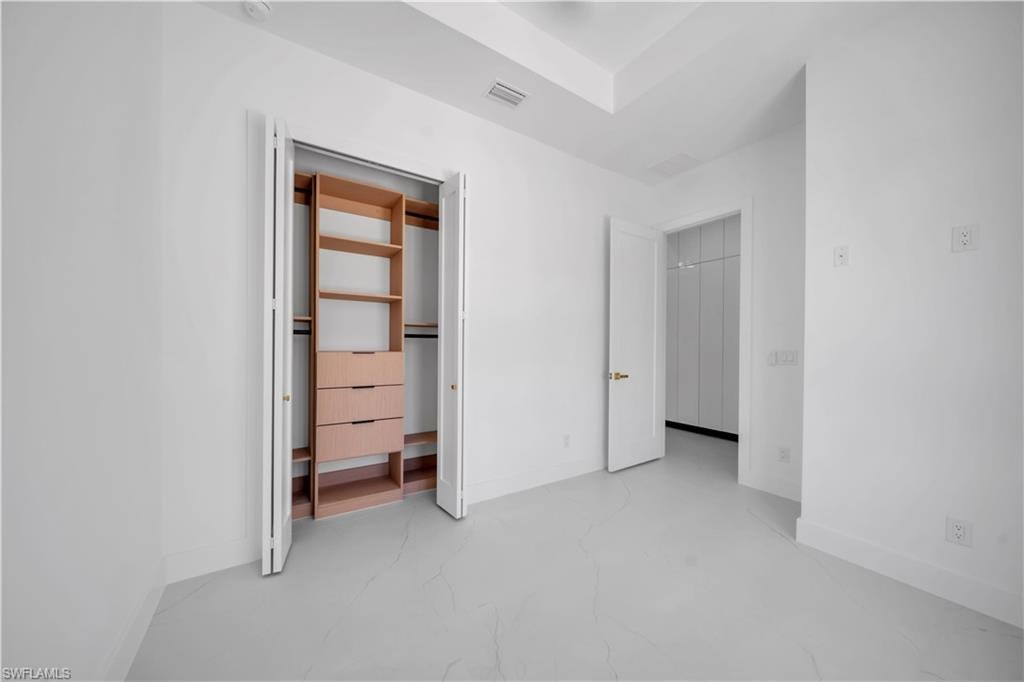 White-painted interior space featuring light-toned flooring, a built-in closet system with shelves and drawers, and a tray ceiling detail