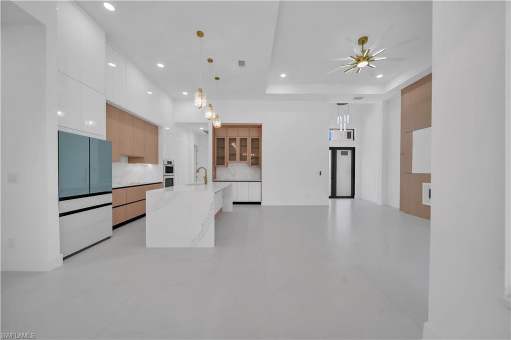 Open-concept living space with a contemporary kitchen featuring a waterfall island, integrated appliances, recessed lighting, and a modern ceiling fan