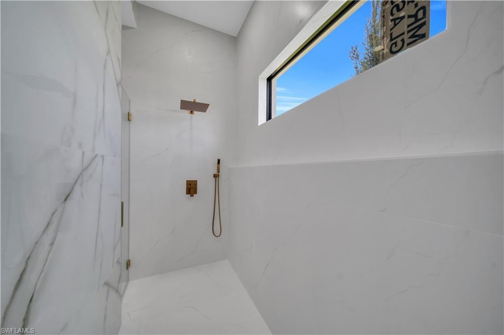 Walk-in shower featuring full-height white tile, a fixed glass panel, bronze-finish fixtures, and a horizontal window
