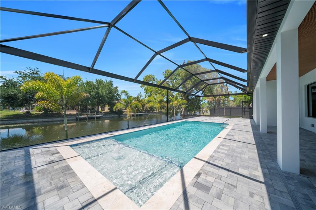 Screened lanai featuring a rectangular pool with sun shelf, paver decking, and a waterfront canal setting