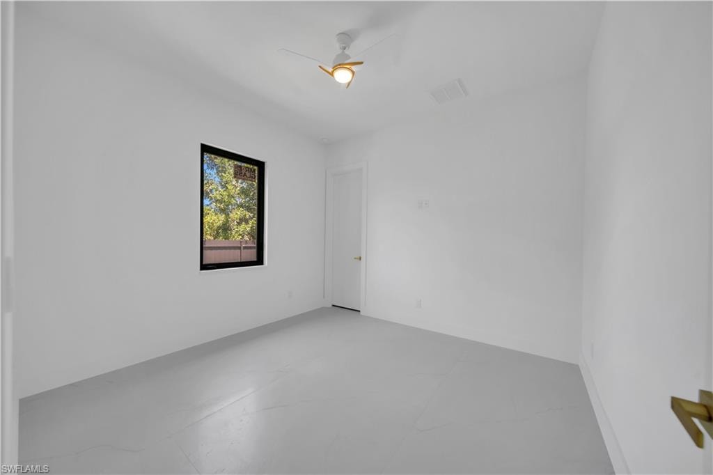 Bright room featuring a single window with dark trim, a white ceiling fan with gold accents, and a white door with a gold handle