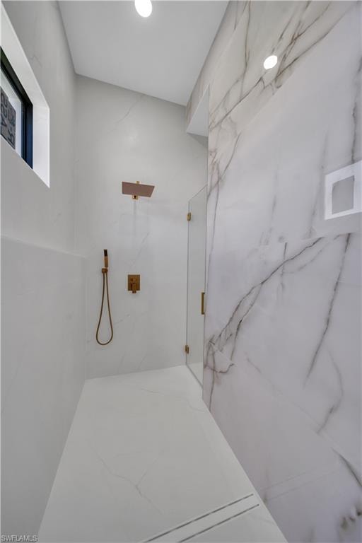 Walk-in shower featuring a rain shower head, hand-held shower fixture, glass enclosure, linear drain, and large format wall tile with veining