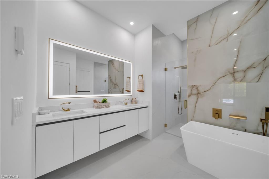 Modern bathroom featuring a dual vanity with white cabinetry, gold-finish hardware, and a lighted mirror