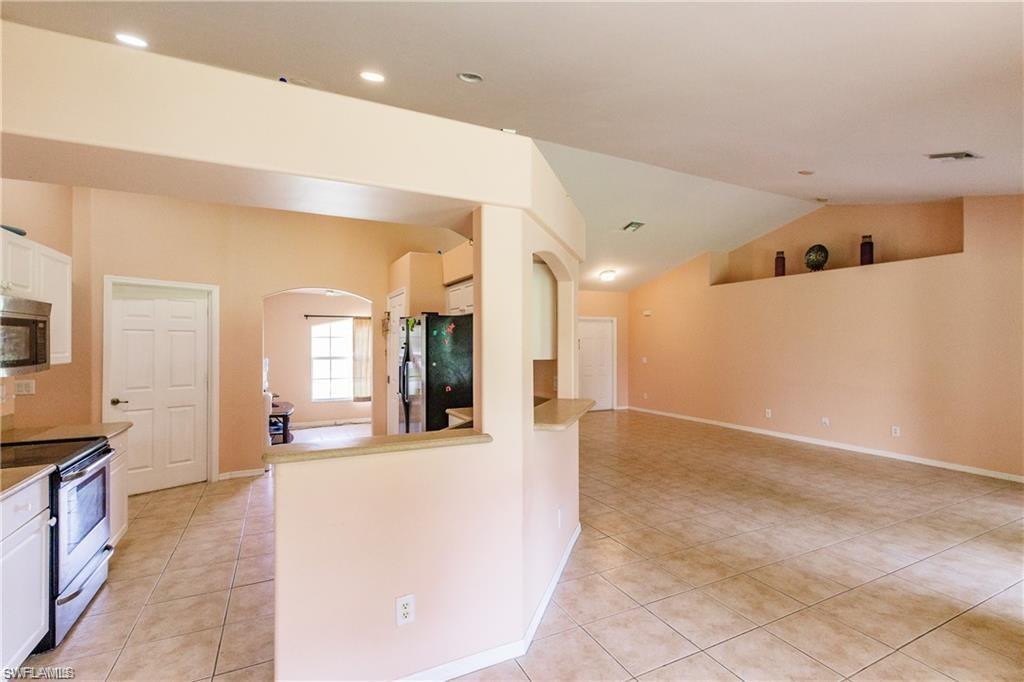 Kitchen with light tile patterned floors, arched walkways, stainless steel appliances, white cabinetry, and vaulted ceiling