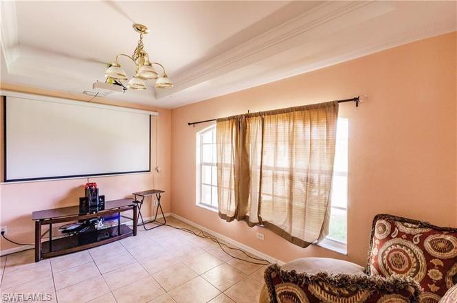 Tiled home theater featuring a raised ceiling, a chandelier, and ornamental molding