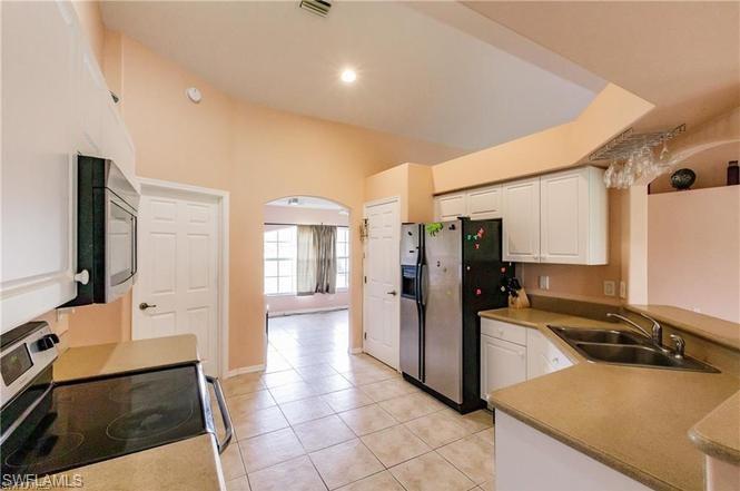 Kitchen with stainless steel appliances, light tile patterned flooring, white cabinets, light countertops, and a peninsula