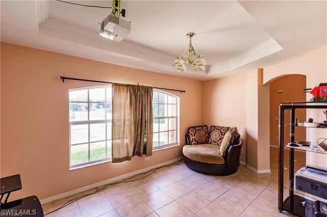 Sitting room with a raised ceiling, crown molding, tile patterned flooring, a chandelier, and arched walkways