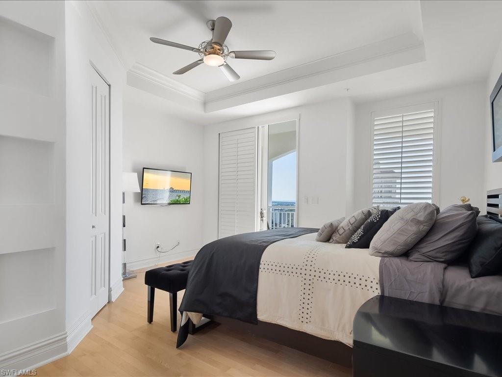 Bedroom with light wood-type flooring, ornamental molding, access to exterior, ceiling fan, and a tray ceiling