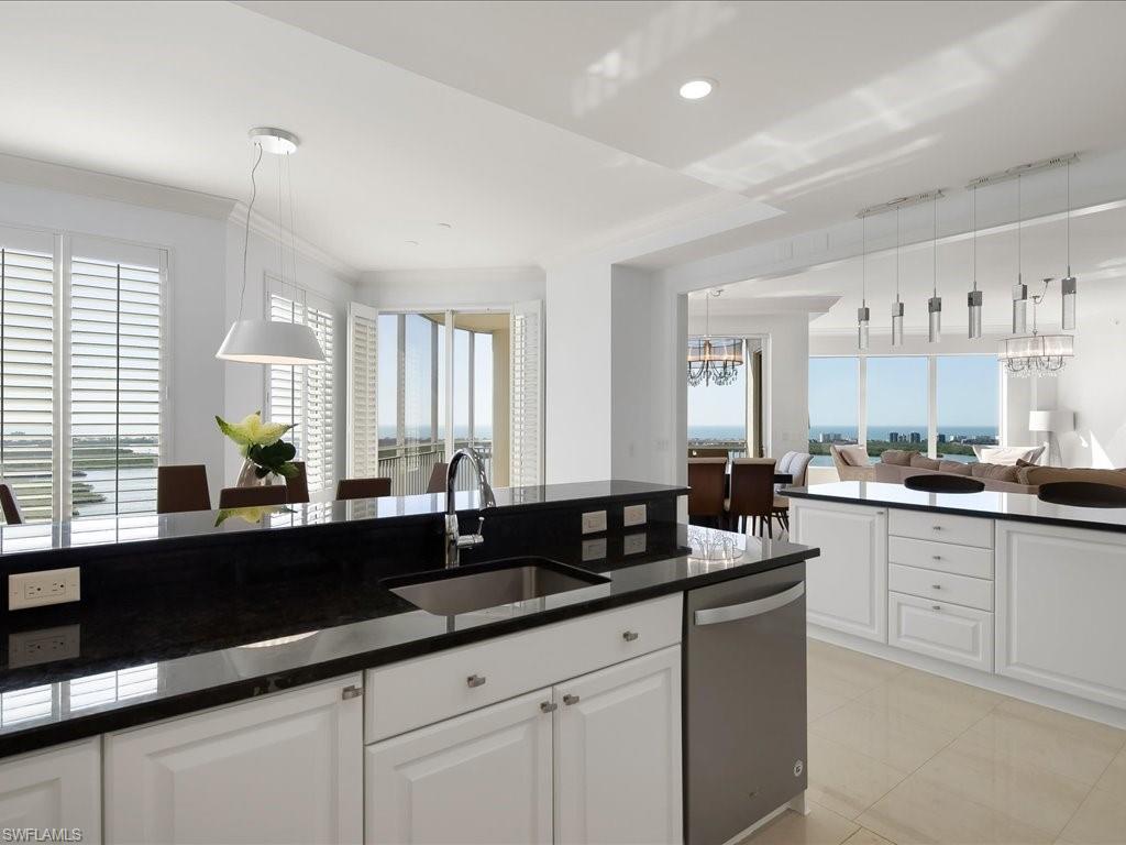 Kitchen featuring white cabinets, stainless steel dishwasher, pendant lighting, a chandelier, and dark stone countertops