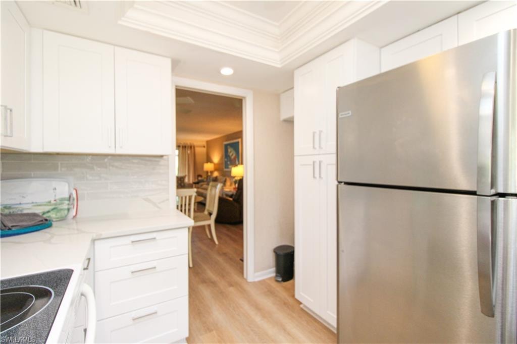 Kitchen with tasteful backsplash, light hardwood / wood-style flooring, white cabinets, and stainless steel refrigerator