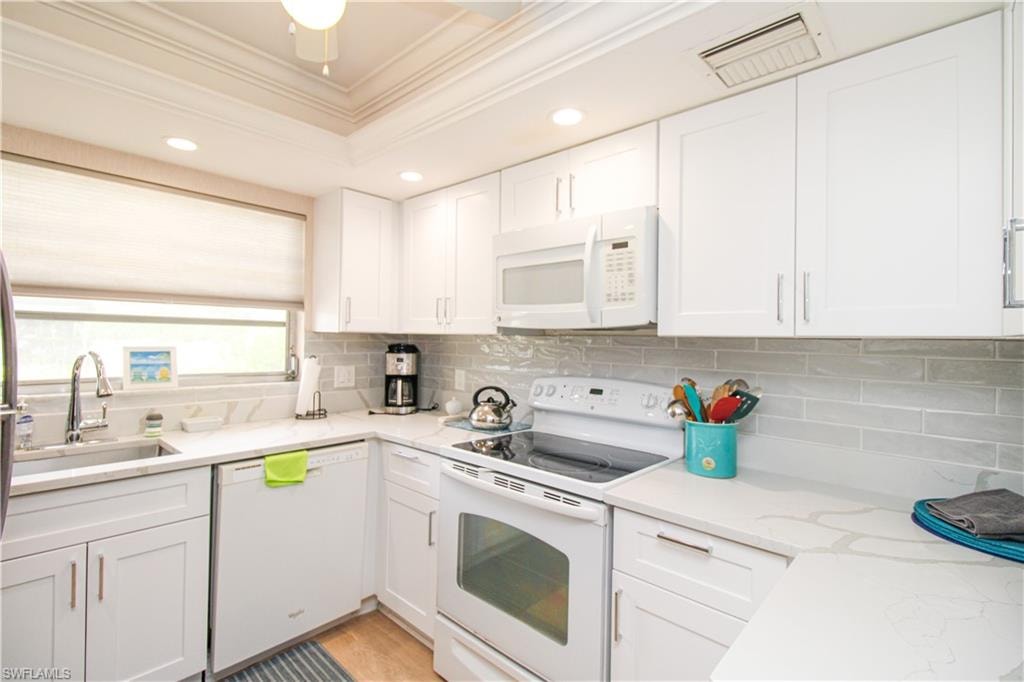 Kitchen featuring white appliances, decorative backsplash, light wood-type flooring, sink, and white cabinetry