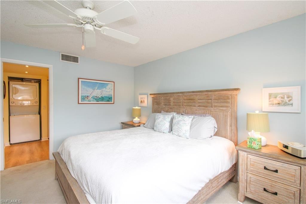 Carpeted bedroom with ceiling fan and stacked washing maching and dryer