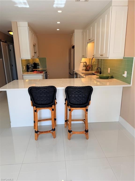 Kitchen with tasteful backsplash, a kitchen breakfast bar, white cabinets, range, and a peninsula