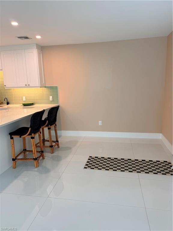 Kitchen with a breakfast bar, decorative backsplash, white cabinets, light stone countertops, and light tile floors