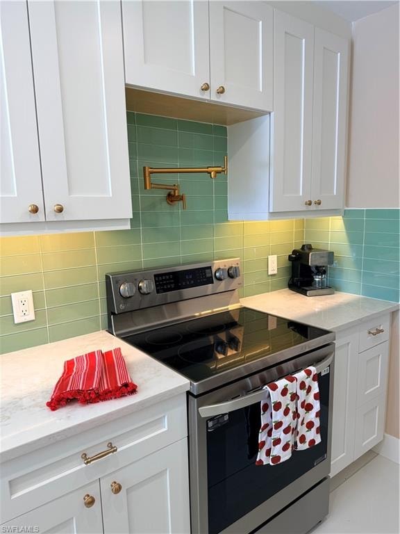 Kitchen with electric range, white cabinets, light stone counters, tile acksplash and pot filler in gold accents