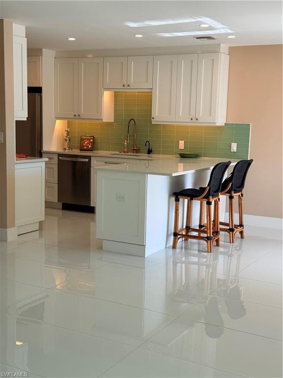 Kitchen featuring white cabinetry, dishwashing machine, a breakfast bar area, tasteful backsplash, and a peninsula
