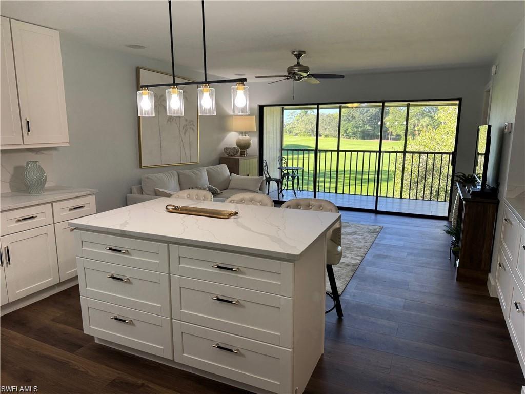 Kitchen featuring white cabinetry, a kitchen breakfast bar, open floor plan, pendant lighting, and light stone counters
