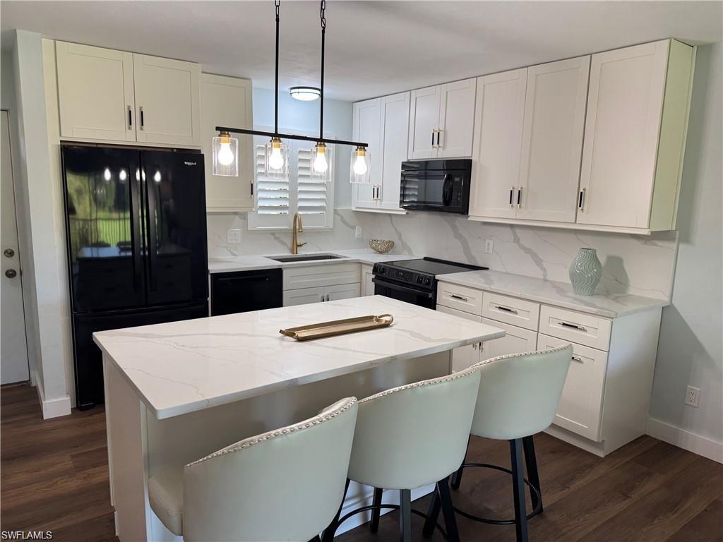 Kitchen featuring black appliances, light stone counters, hanging light fixtures, white cabinetry, and a kitchen bar