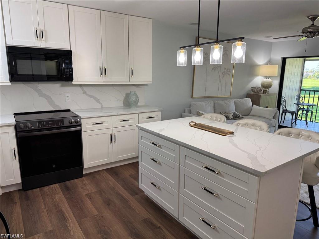 Kitchen with electric range, a breakfast bar, black microwave, white cabinets, and open floor plan