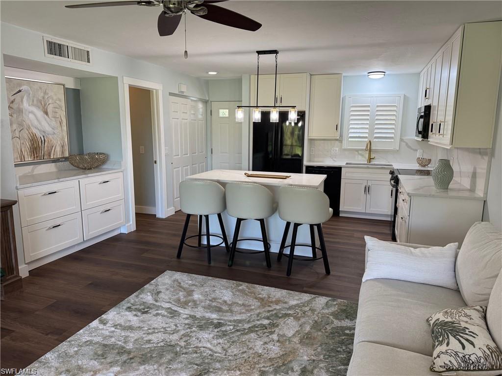 Kitchen featuring white cabinetry, black appliances, hanging light fixtures, a center island, and light stone countertops