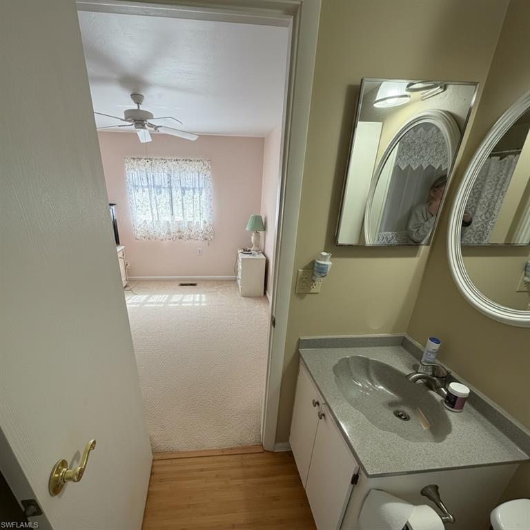 Bathroom with vanity, ceiling fan, light carpet, and light wood-style floors