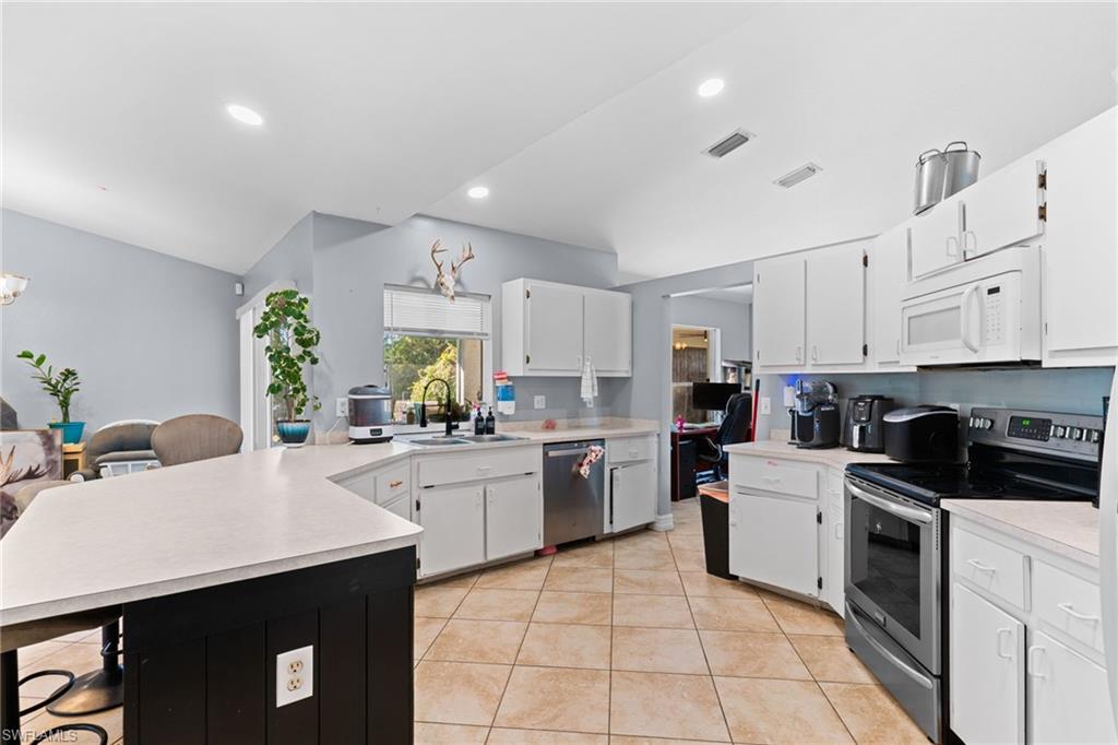 Kitchen with a breakfast bar area, stainless steel appliances, white cabinets, light countertops, and recessed lighting