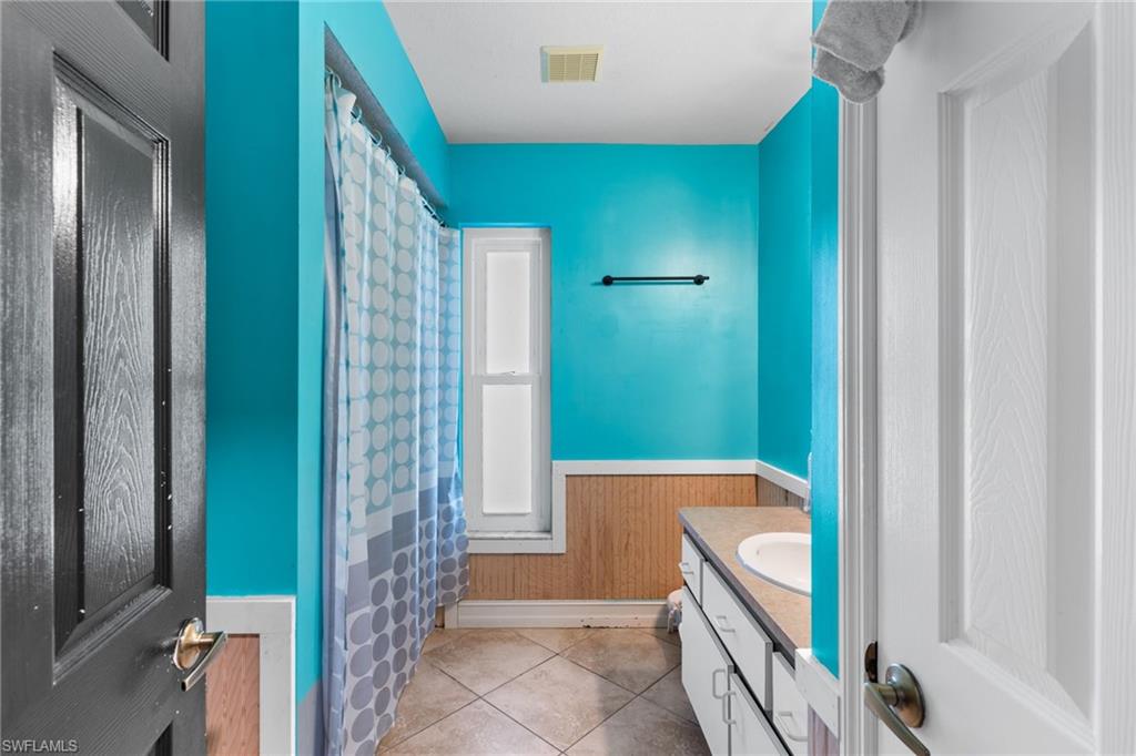 Full bathroom featuring vanity, wainscoting, a shower with shower curtain, light tile patterned floors, and wooden walls