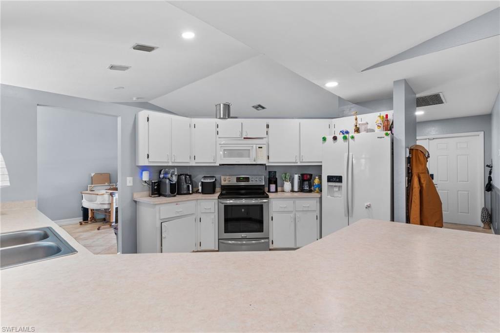 Kitchen featuring lofted ceiling, white cabinetry, light countertops, and white appliances