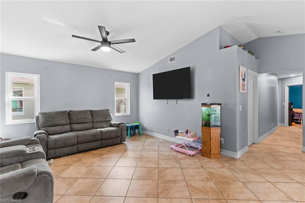 Living area with lofted ceiling, ceiling fan, light tile patterned floors, and healthy amount of natural light