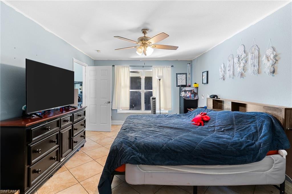 Bedroom with light tile patterned floors, ceiling fan, and crown molding