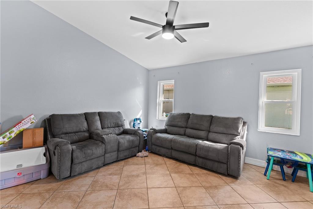 Living room featuring healthy amount of natural light, light tile patterned floors, a ceiling fan, and lofted ceiling