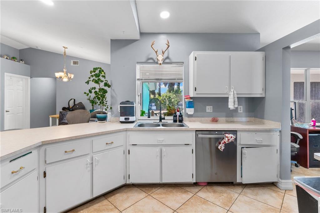 Kitchen with white cabinets, light countertops, stainless steel dishwasher, decorative light fixtures, and light tile patterned flooring