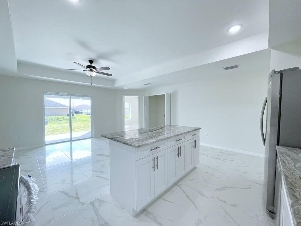 Kitchen featuring light stone counters, freestanding refrigerator, a kitchen island, open floor plan, and ceiling fan