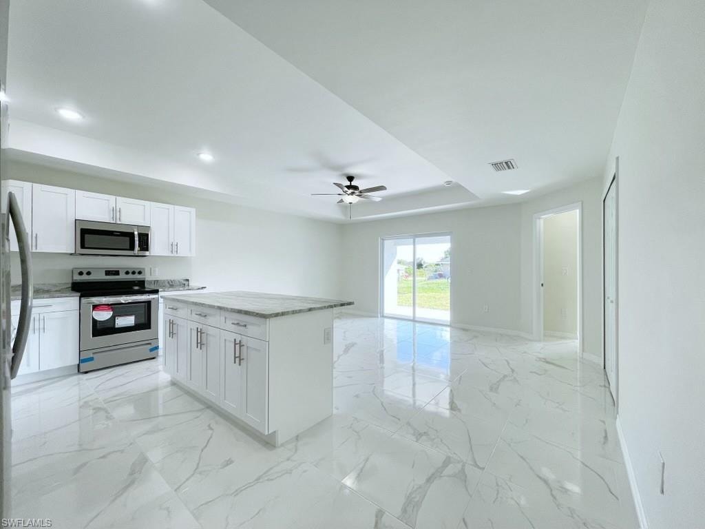 Kitchen featuring stainless steel appliances, a center island, light stone countertops, white cabinets, and a ceiling fan