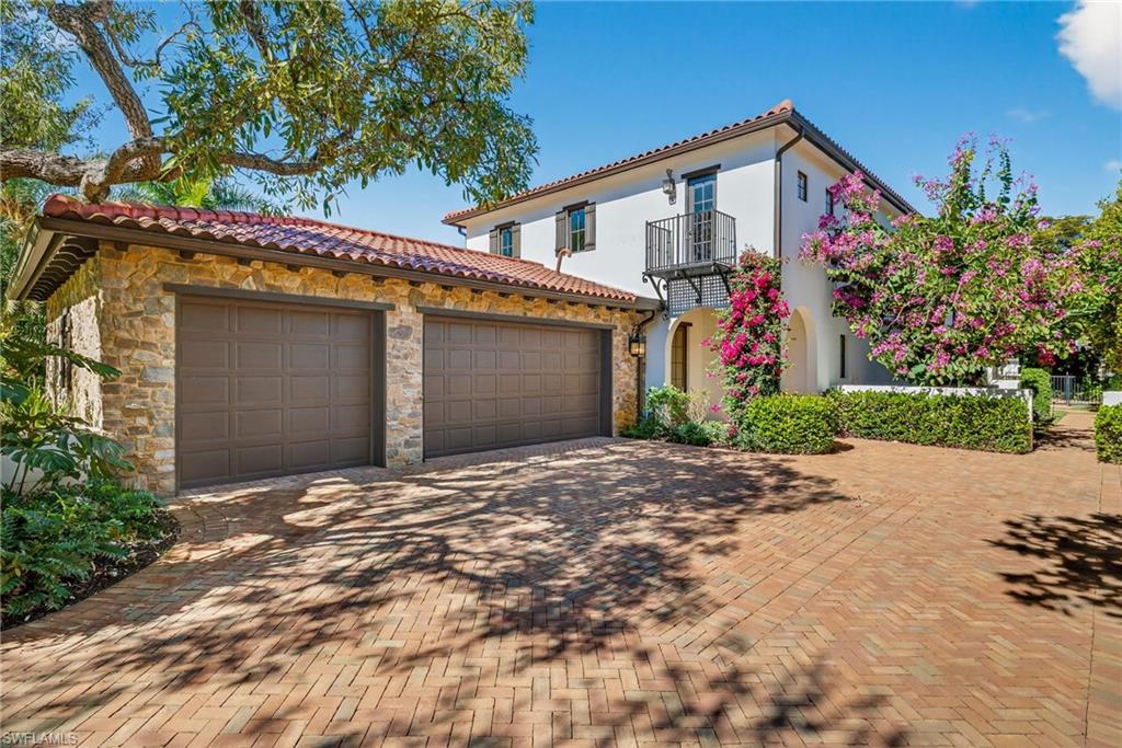 Mediterranean / spanish house featuring a balcony, decorative driveway, a tile roof, stone siding, and an attached garage