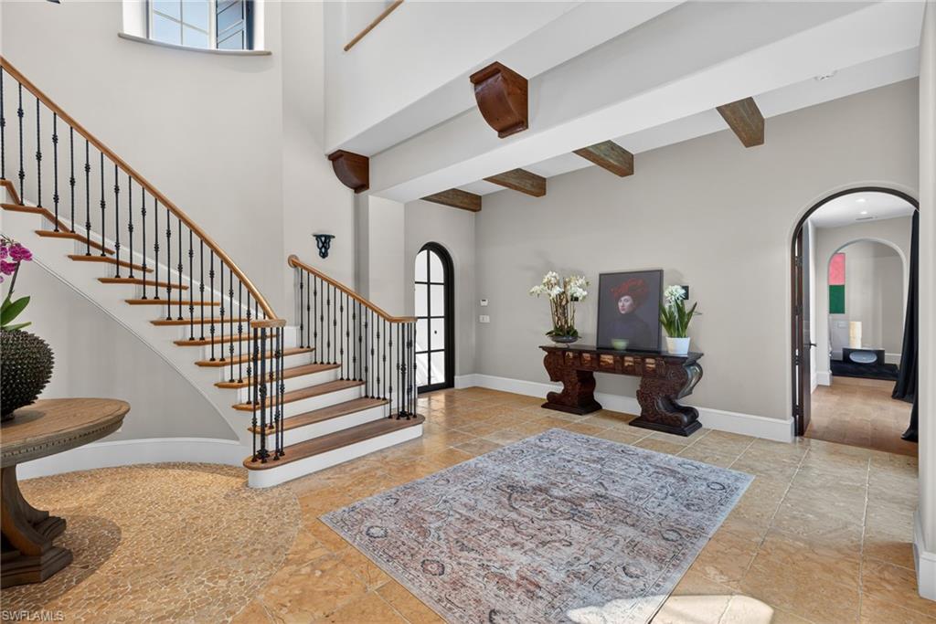 Foyer with arched walkways, stairway, beam ceiling, and a high ceiling