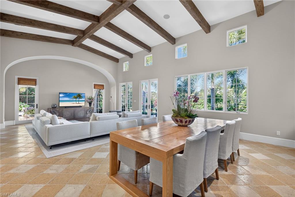 Dining area with beam ceiling, high vaulted ceiling, and stone tile flooring
