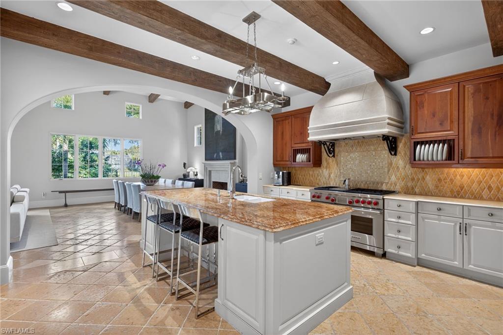 Kitchen featuring backsplash, premium range, arched walkways, a breakfast bar, and premium range hood