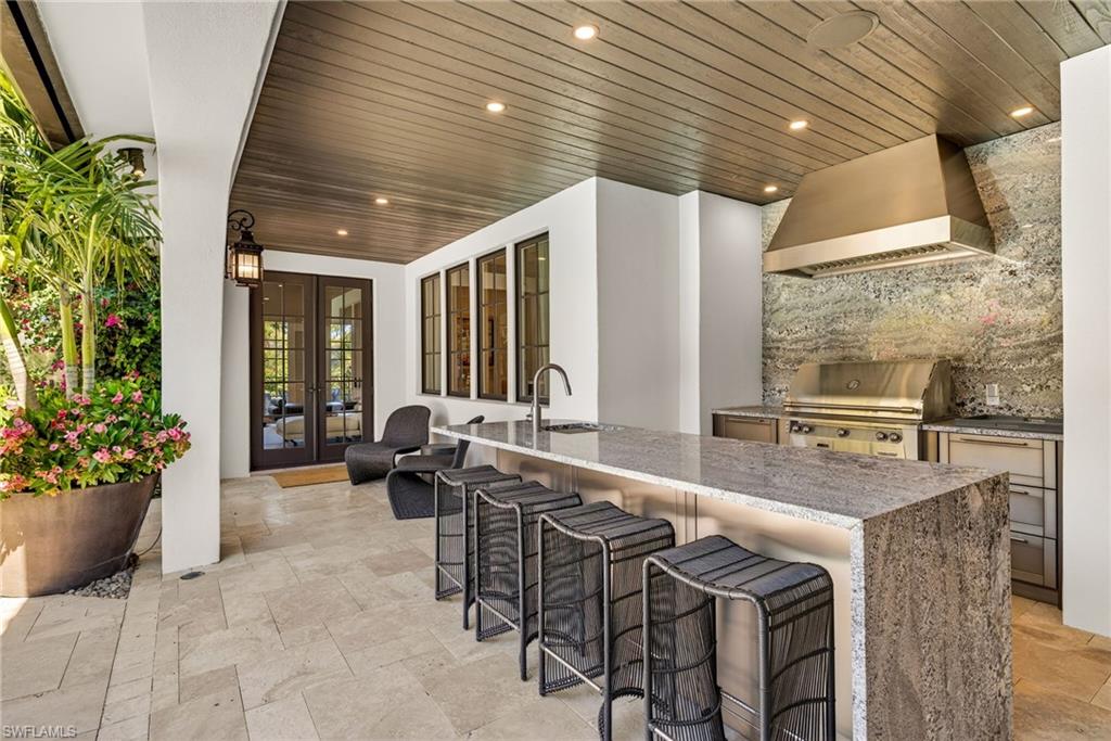 Kitchen with french doors, custom exhaust hood, stone tile floors, light stone countertops, and a kitchen breakfast bar