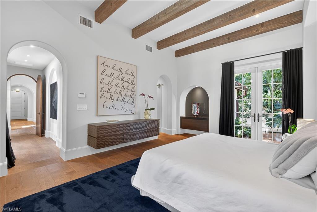 Bedroom featuring light wood-style flooring, beam ceiling, arched walkways, and french doors